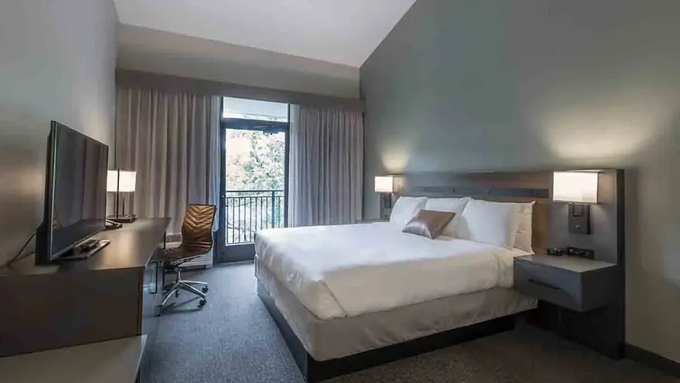 Modern hotel room with a king bed, desk, and balcony view.