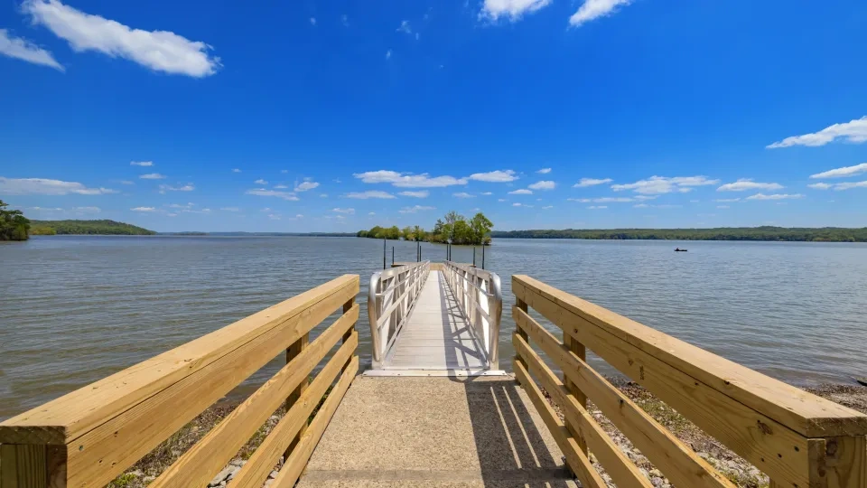 Wooden pier extending into a calm lake under a bright blue sky with clouds.