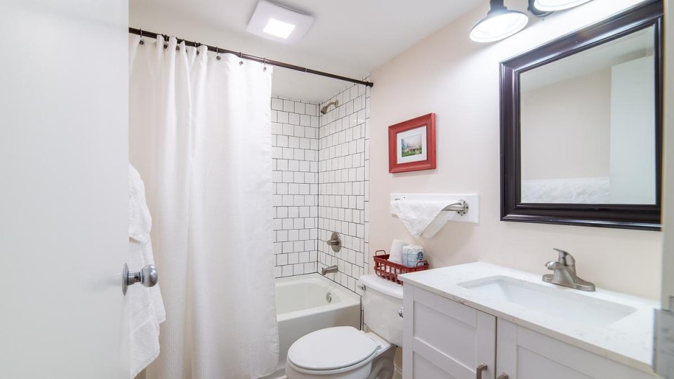 White bathroom with overhead lighting, shower tub, toilet, sink with counter space, towels, and a mirror