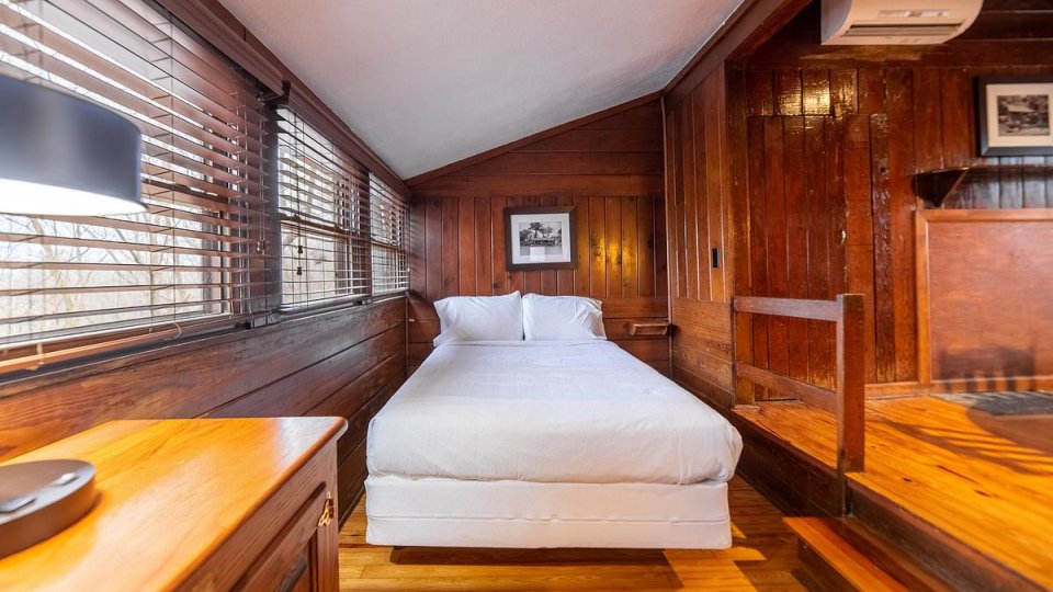 Wooden room with one bed, windows, wooden railing, and a air conditioner