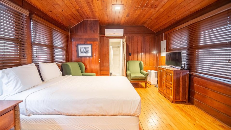 Wooden bedroom with one bed, a night stand, chairs, a cabinet, windows, air condition, and a television