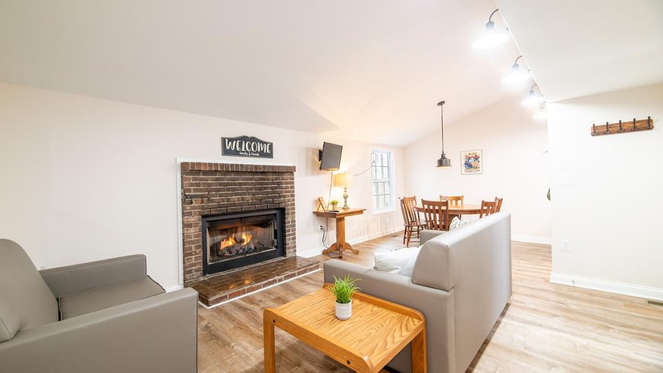 Living room with overhead lighting, a fireplace, a couch, a chair, wooden tables, and wooden chairs