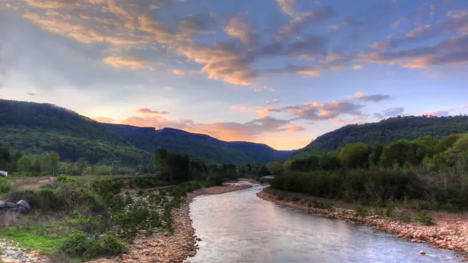 River winds through a lush valley at sunset, under colorful clouds.