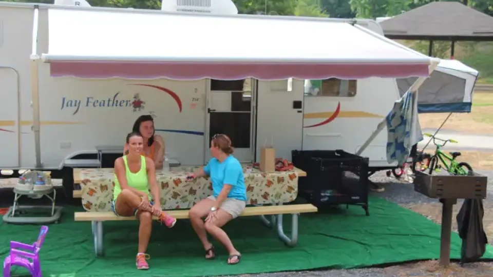 Three people sitting outside a camper on a picnic table, under an awning.