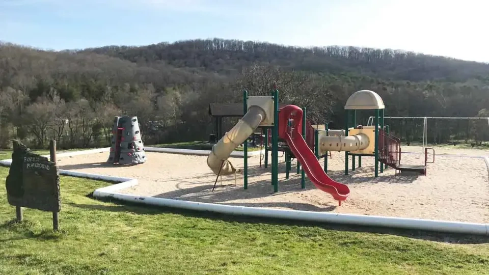Playground with slides and climbing structures surrounded by scenic hills.