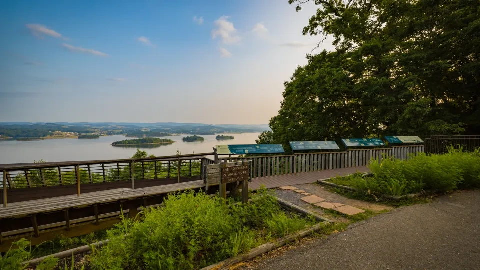 Scenic lake view from overlook deck with trees and informational signs.