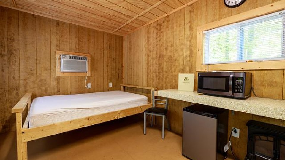Wooden room with air conditioner, bed, mini fridge, microwave, window, chair, and clock