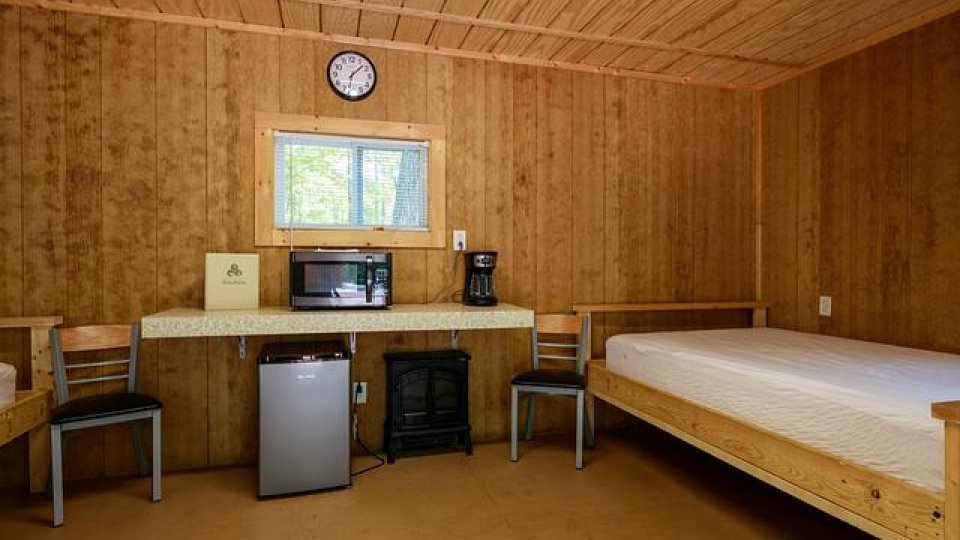wooden room with bed, two chairs, mini fridge, coffee maker, microwave, window, and clock