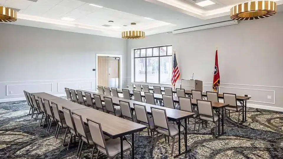 Conference room with arranged chairs, two flags, and elegant lighting.