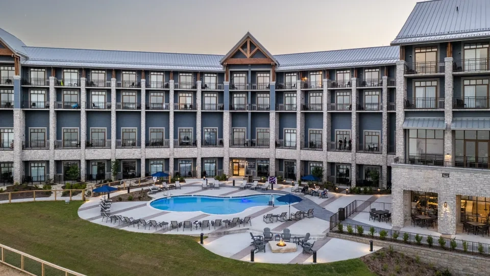 Hotel courtyard with pool, surrounded by lounge chairs and fire pit, under a clear sky.