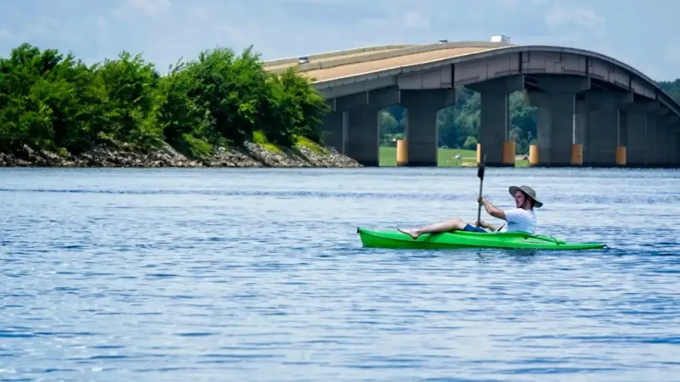 Person kayaking on a lake near a bridge under a clear sky.