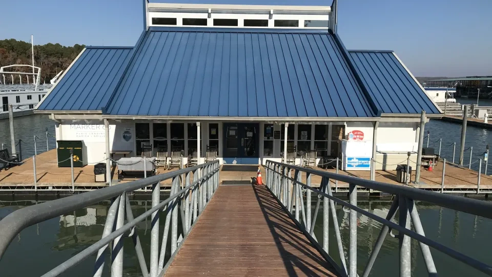 Wooden dock leading to a building with a blue roof on the water.