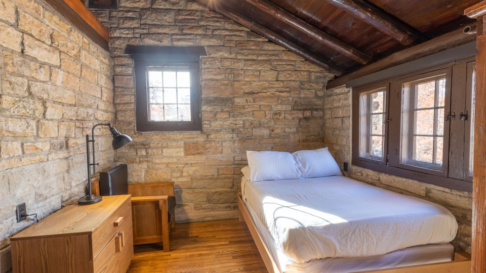 second room with full bed and dresser with desk lamp, small window