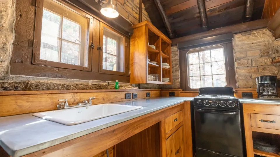 Rustic kitchen with stone walls, wooden cabinets, and a black stove.