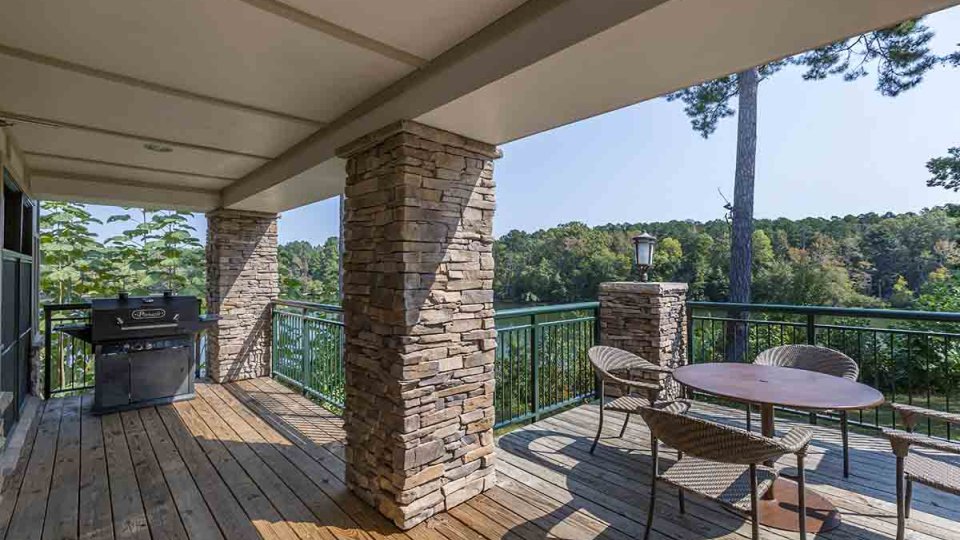 Patio thats half covered, grill, stone pillars, railing, table, and chairs