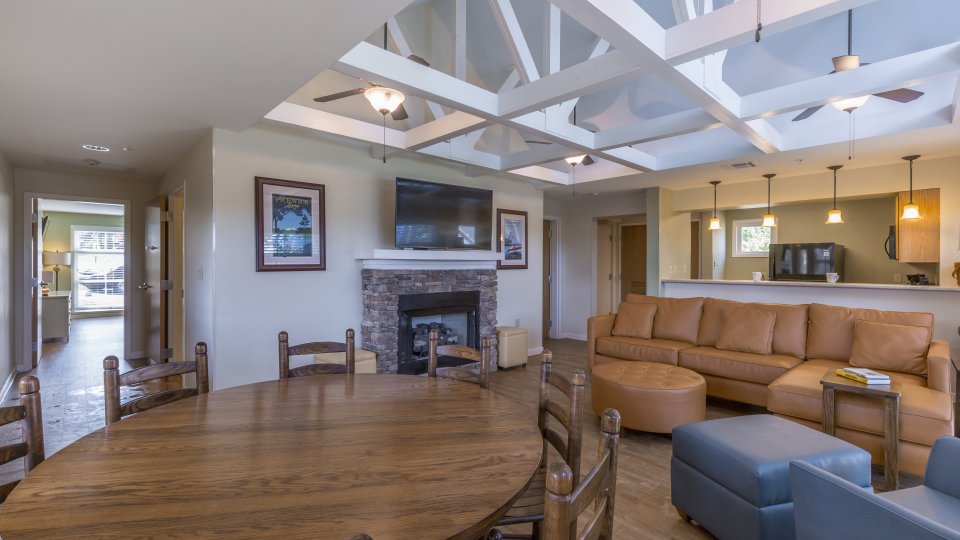 living room with ceiling fans, dining table, couch, chairs, cushioned chair, foot rests, fireplace, television, and overhead lighting