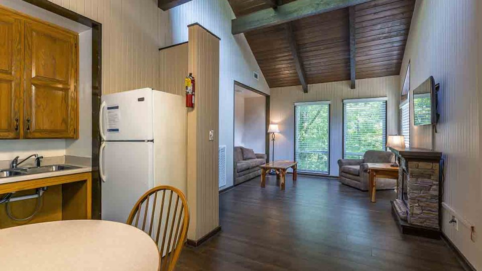 open room showing a kitchen and living room, fridge, fireplace, mounted television, couch, and cushioned chair