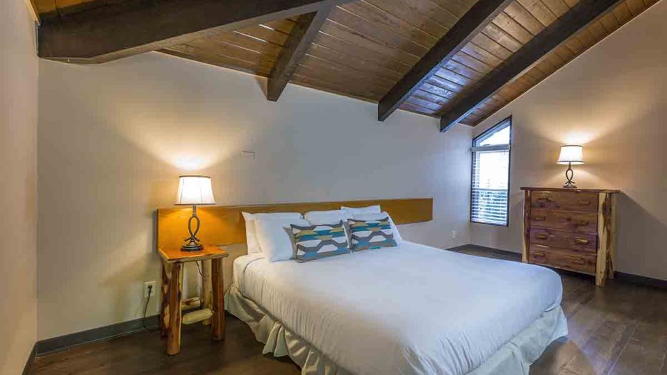 Bedroom with one bed, nightstand with lamp on top, dresser with lamp on top, and a window in the corner