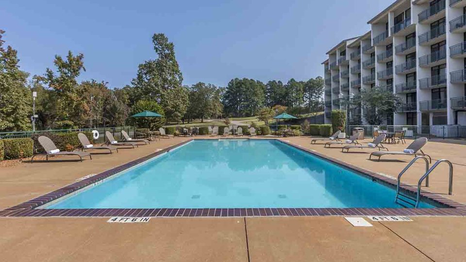 Swimming pool that has pool chairs, umbrellas, with a building on the right