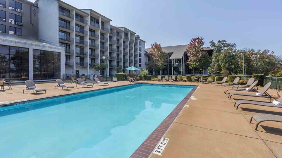 Pool that has pool chairs surrounding the pool with a building on the left and in the distance