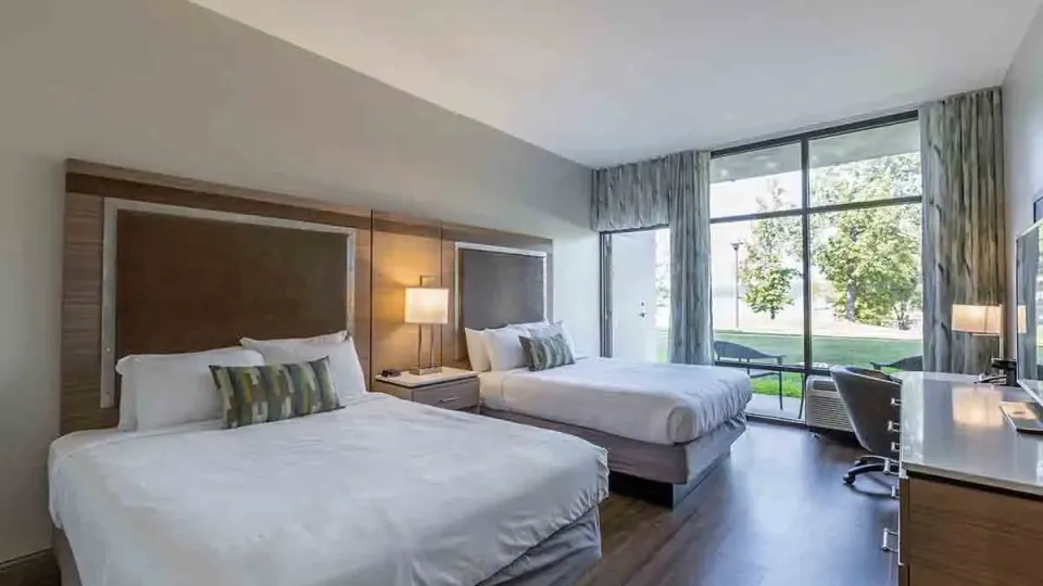Hotel room with two beds, large window, and nature view.