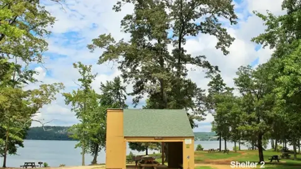 Shelter by a lake surrounded by trees under a blue sky.
