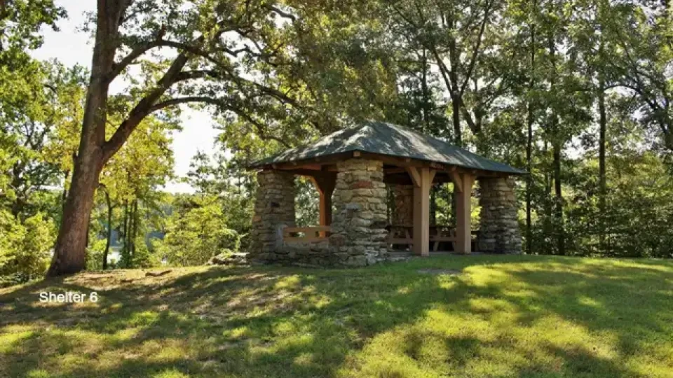 Stone shelter surrounded by trees on a sunny day.