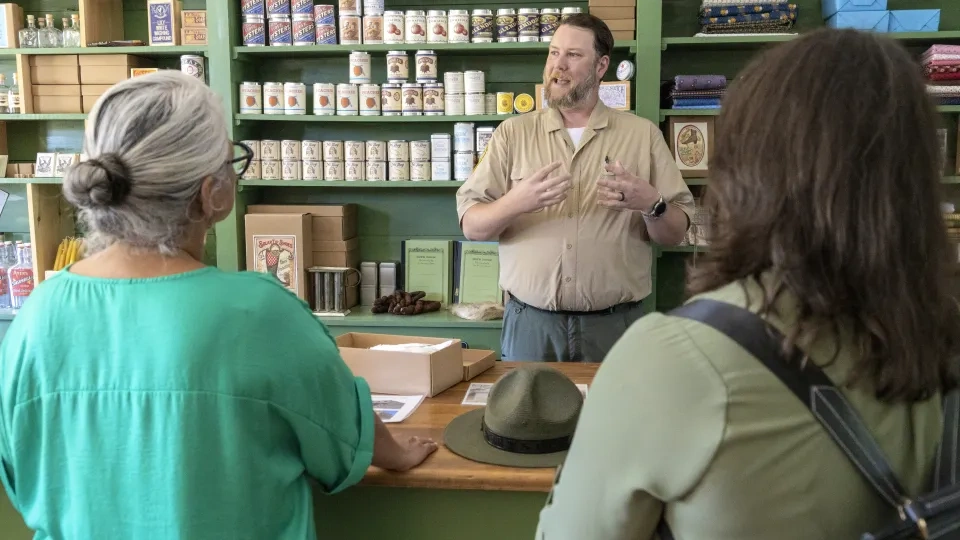 Man explaining in a vintage store with canned goods and customers listening.