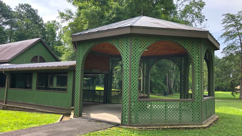 Green gazebo with lattice walls in a park setting.