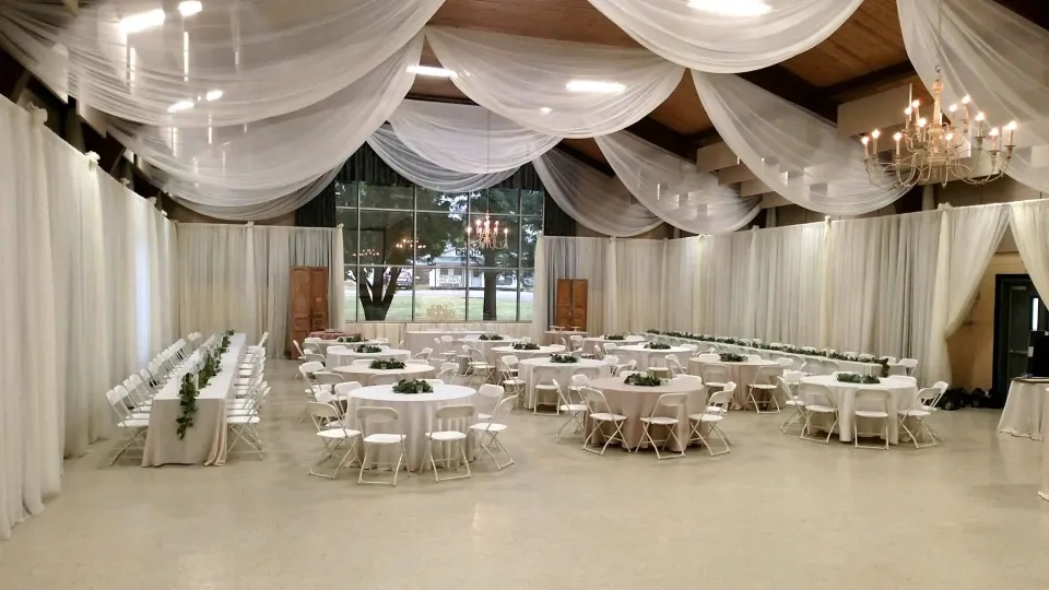 Elegant hall with round tables, white chairs, and draped ceilings.