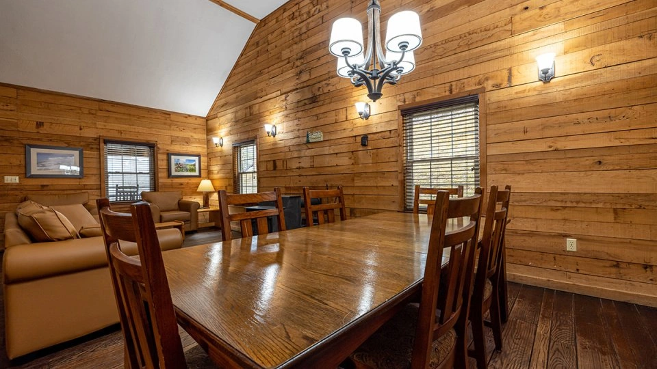 Dining area in a Roan Mountain cabin with a wooden table and chairs near large windows.