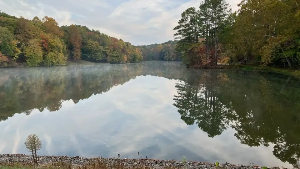 Calm lake with autumn trees reflecting on the water, grassy foreground.