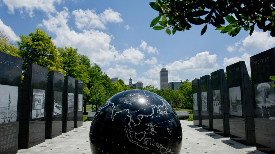 Black globe sculpture surrounded by tall engraved panels and trees under a blue sky.