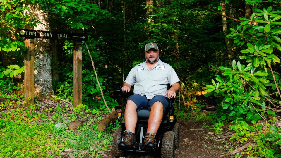man sitting in all terrain wheel chair that is on a natural trail
