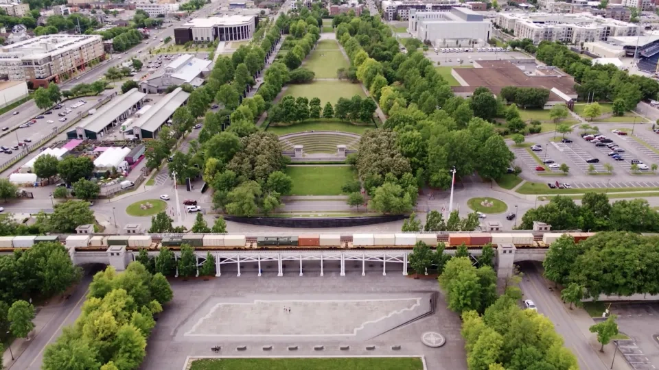 Aerial view of a city park with train tracks and surrounding buildings.
