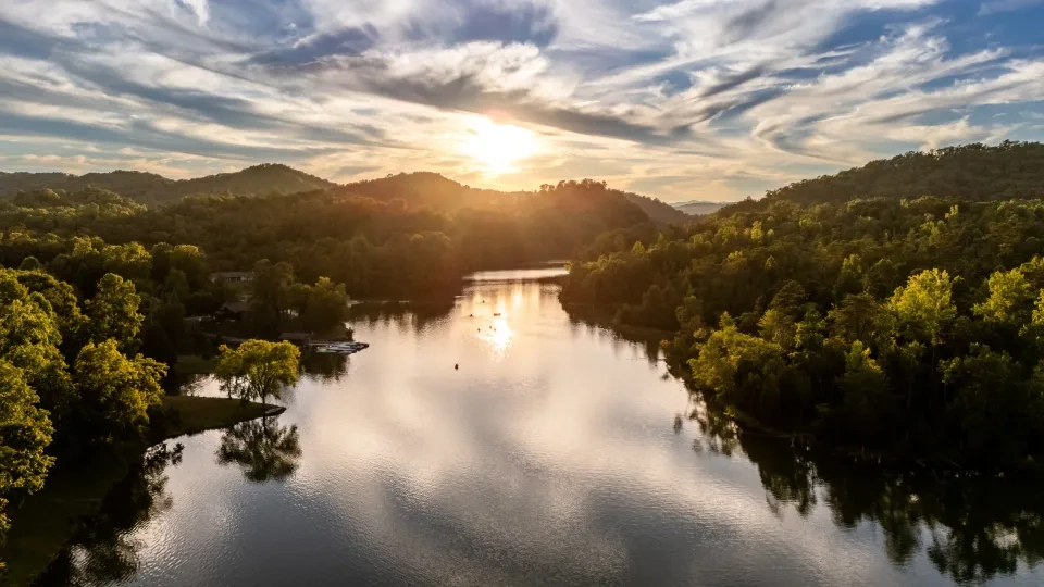 Sunset over a tranquil lake surrounded by lush green hills and dramatic clouds.