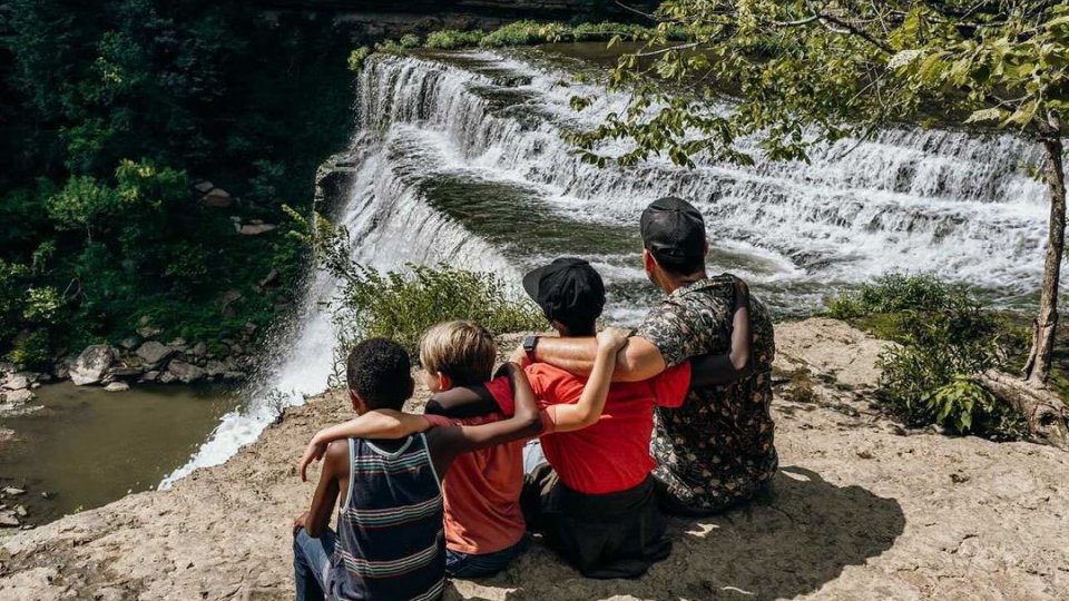 4 people sitting on a ledge overlooking a waterfall at burgess falls state park