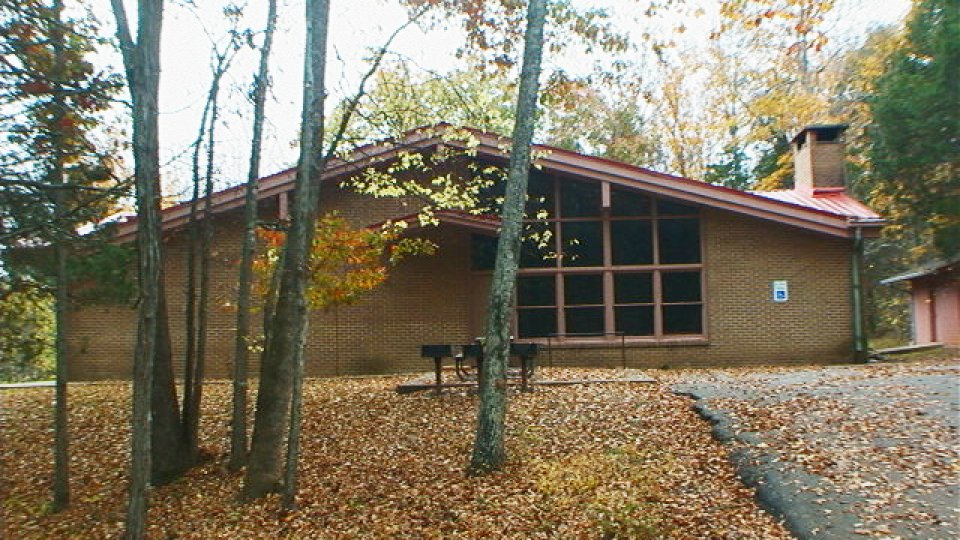 Brick building with large windows, surrounded by autumn trees and a blanket of fallen leaves. A peaceful, rustic outdoor setting.