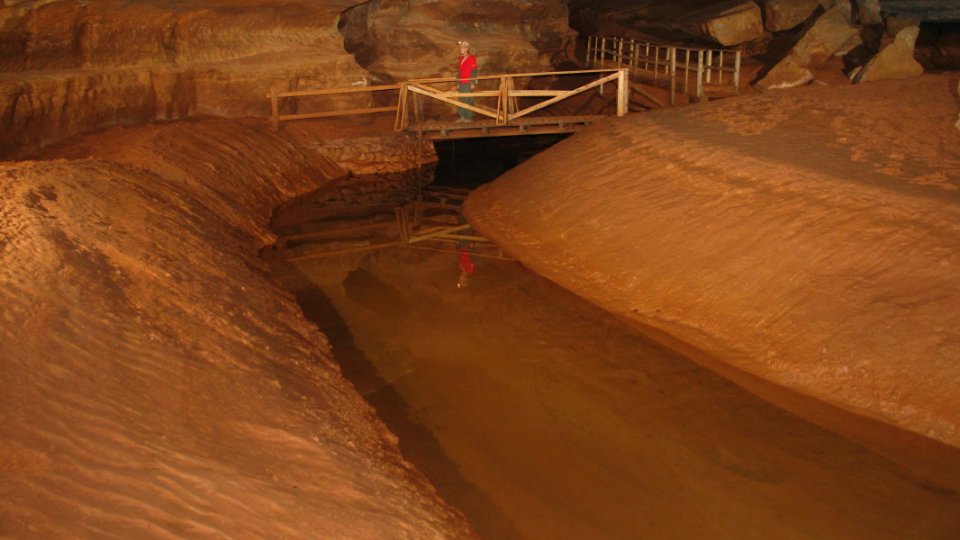 person walking through dunbar cave over a bridge with a helmet on