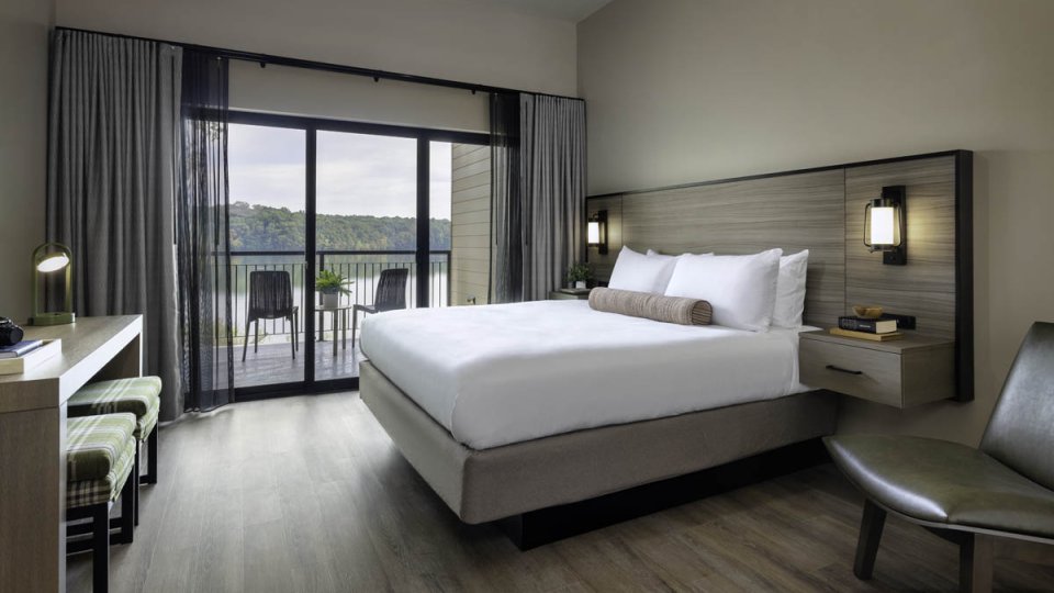 Bedroom with a king bed, wooden floor and bed frame, modern lighting and a glass door leading to a patio