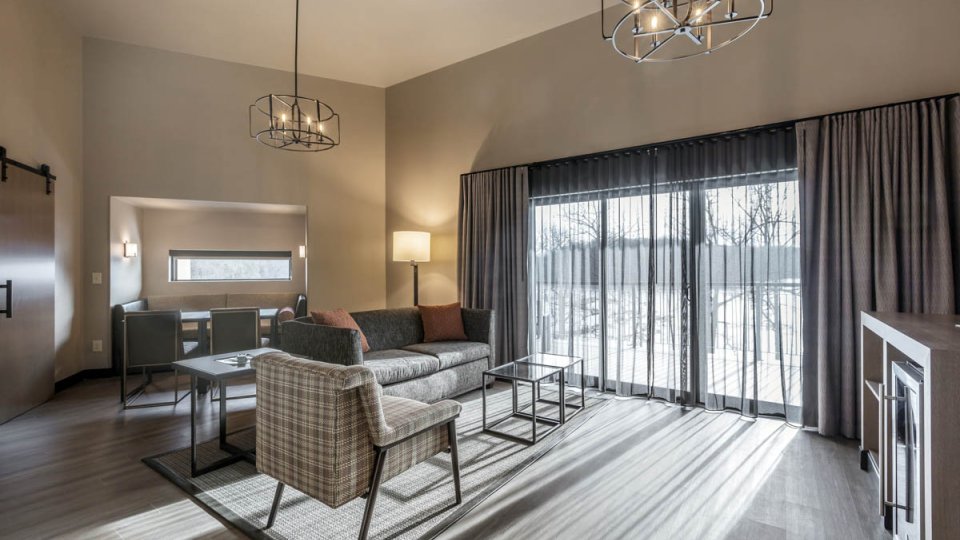 Suite room with a glass coffee table, chairs , a couch a counter with a fridge underneath and a glass door leading to the patio