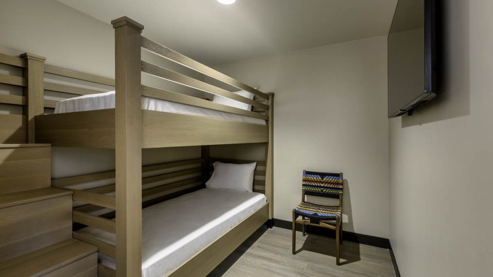 Children bedroom with bunk beds, stairs leading to the top bunk, a chair along the wall, and a television across from the beds