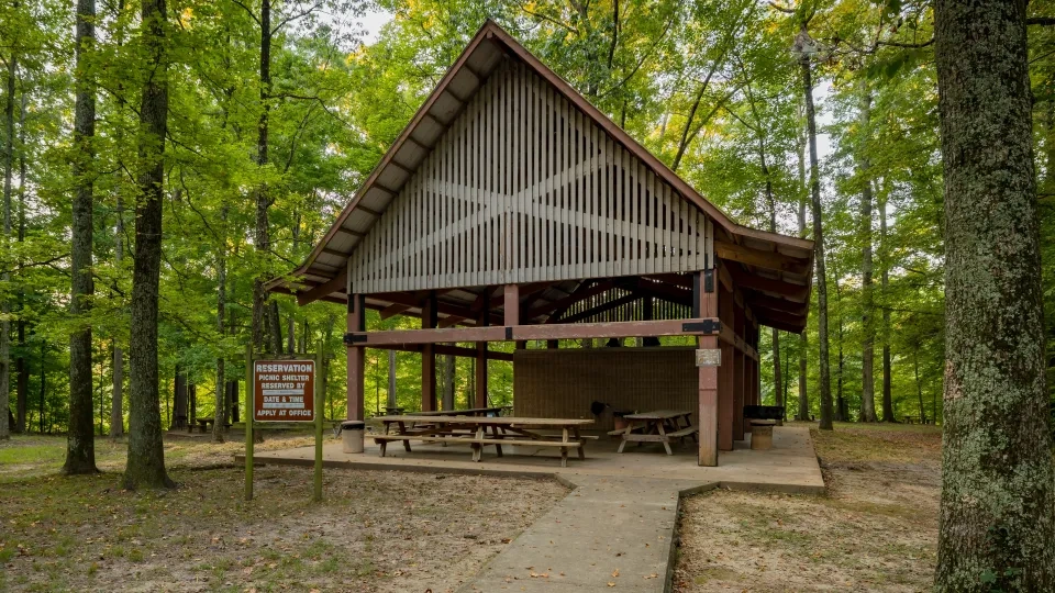 Wooden picnic shelter in a forest with tables and a reservation sign.