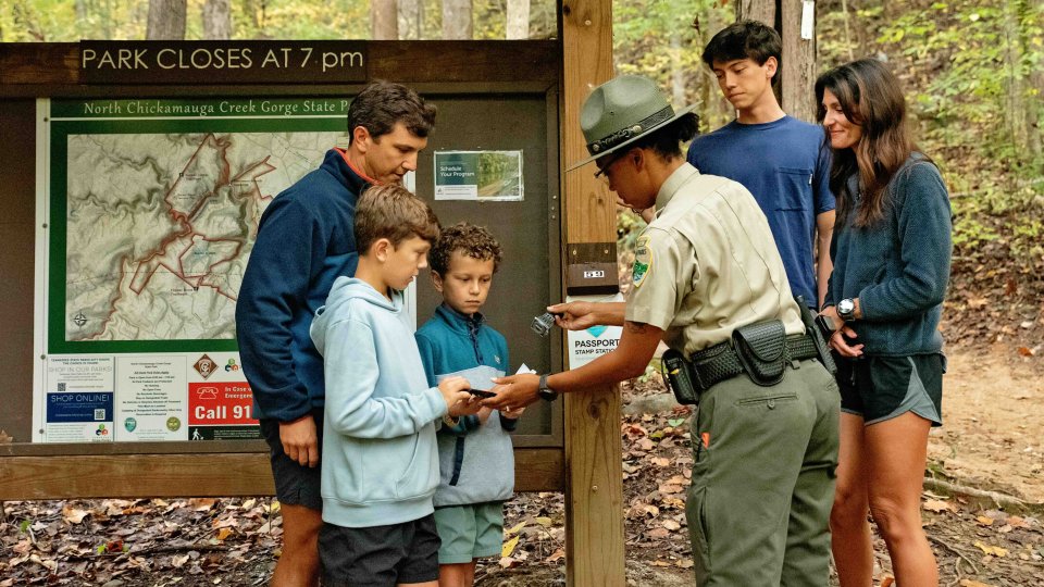ranger with family stamping a book a child is holding