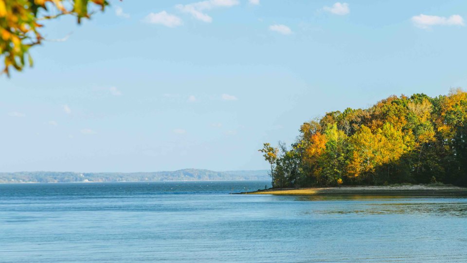 view of water with some patches of land with trees and mountains in the distance