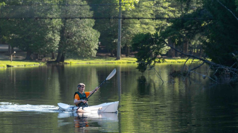 man paddling in a boat on calm water with a bridge above him