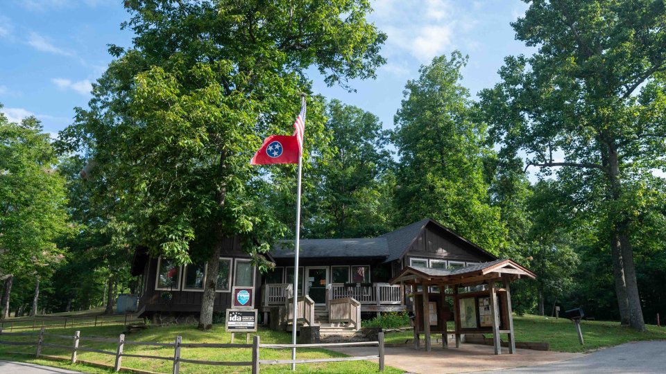 wooden building with a flag pole in front flying the Tennessee flag, and a small shelter with park information in front