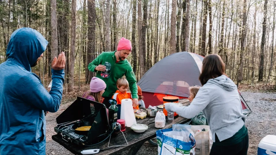 Family cooking at a campsite with a tent and trees in the background.