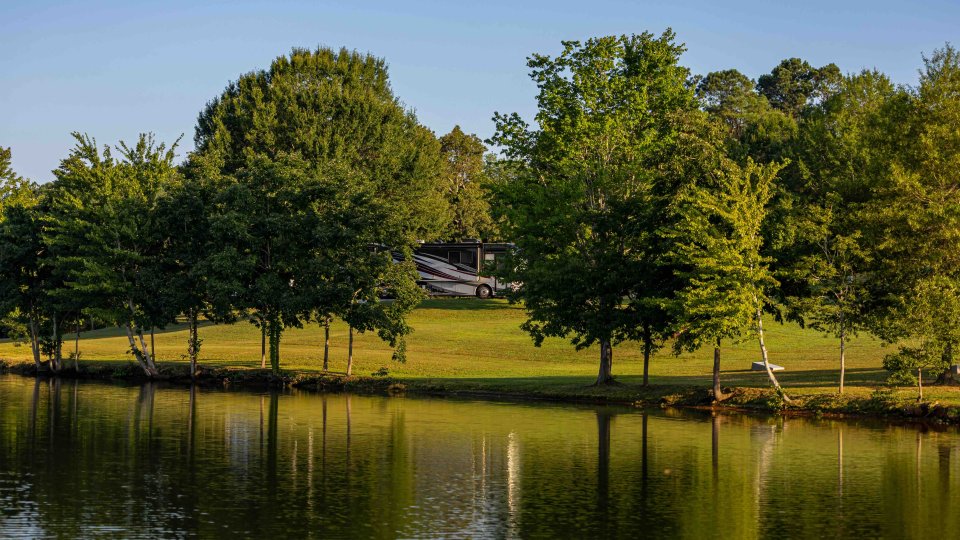 view of lake and across the water is land with some trees and an RV parked