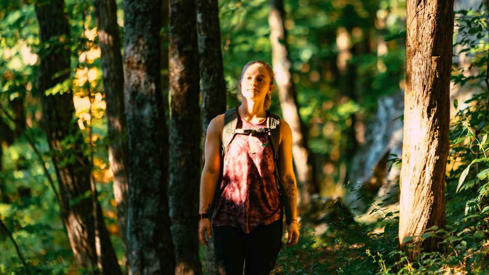 girl hiking in forest wearing a backpack and sun shining on her